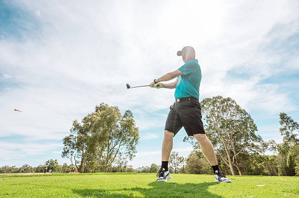 istock Man in golf clothing swinging on a lush green golf course surrounded by trees under a clear blue sky 2238804210