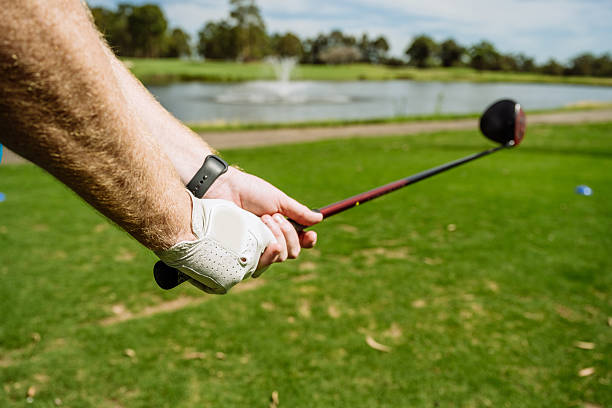 A golfer in a light blue shirt and gray pants is focused on putting on a lush green golf course. The serene setting, with, captured with a three-quarter length portrait, trees in the background, highlights the precision and concentration required in the sport. The scene captures the essence of golf practice and skill development.