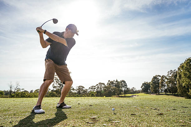 istock Man in golf clothing swinging on a lush green golf course surrounded by trees under a clear blue sky 2238804411