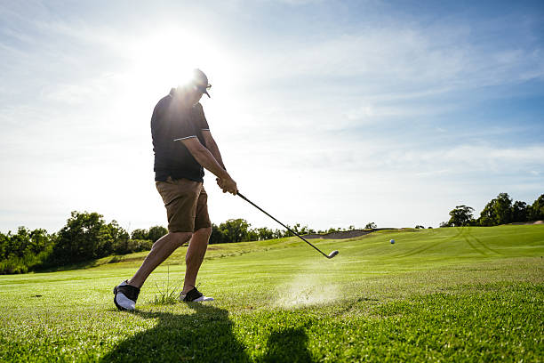 istock Man in golf clothing swinging on a lush green golf course surrounded by trees under a clear blue sky 2238804449