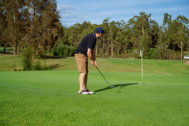 istock Mature golfer in golf clothing putting on a lush green golf course surrounded by trees under a clear blue sky 2238804511
