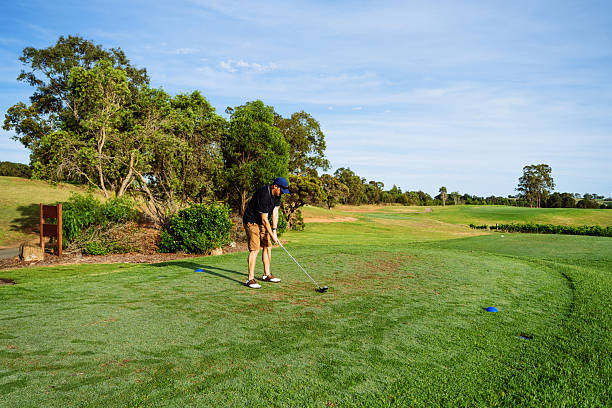 istock Mature golfer in golf clothing putting on a lush green golf course surrounded by trees under a clear blue sky 2238804517
