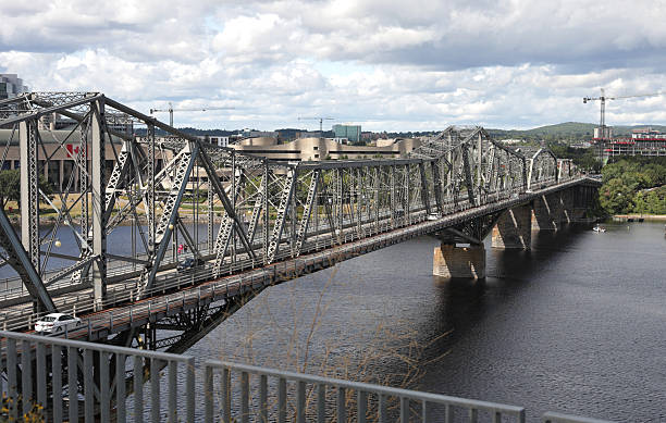 Ottawa, Canada - August 25, 2025: Looking west from Kiweki Point on the Ontario side of the Ottawa River to Gatineau, Quebec. The interprovincial Alexandra Bridge spans the Ottawa River between the two provinces. Pedestrians walk along the Trans Canada Trail. Designated a National Historic Civil Engineering Site. Construction activity in progress near the Canadian Museum of History. Summer morning with clouds over the National Capital Region.