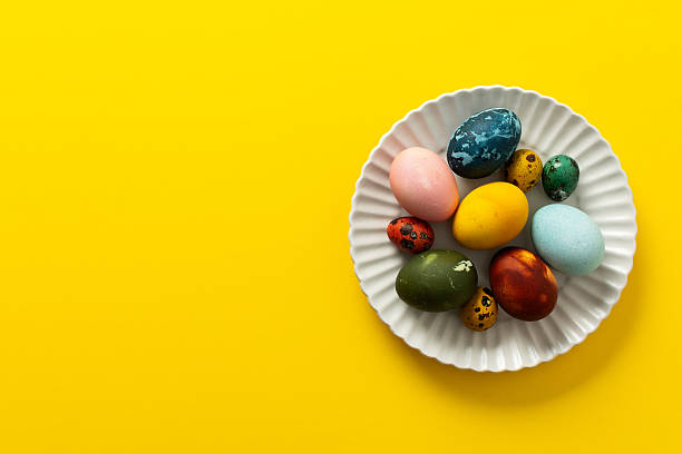 istock A variety of beautifully painted Easter eggs in different colors and patterns are placed on a delicate white plate. The vibrant hues stand out against the cheerful yellow backdrop 2238805889