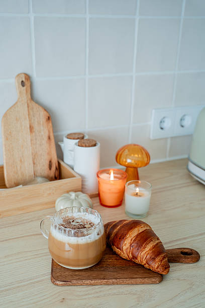 Cup of hot latte with foam, candle, croissant on the table. Autumn drink.