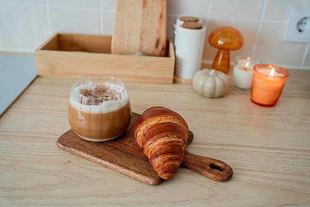 Cup of hot latte with foam, candle, croissant on the table. Autumn drink.