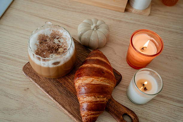 Cup of hot latte with foam, candle, croissant on the table. Autumn drink.