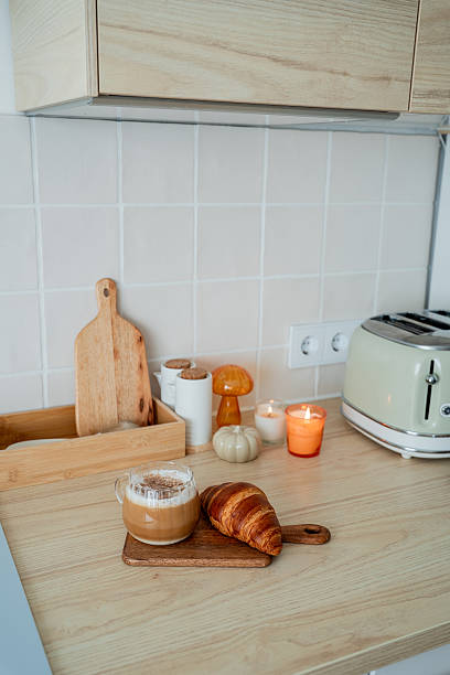 Cup of hot latte with foam, candle, croissant on the table. Autumn drink.