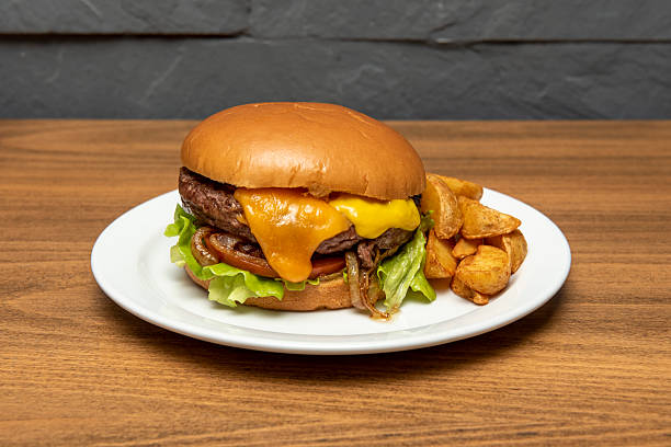 istock Beef burger with melted cheddar cheese, mustard, fried onion, tomato and lettuce and garnish of fried potato wedges 2238816598