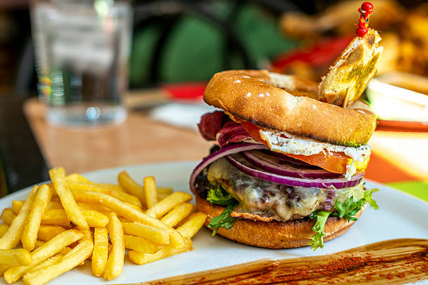 istock Beef burger with fried egg, crispy red onion rings, melted cheese, fried bacon, raw lettuce, tomato slices and a side of fried potatoes 2238822667