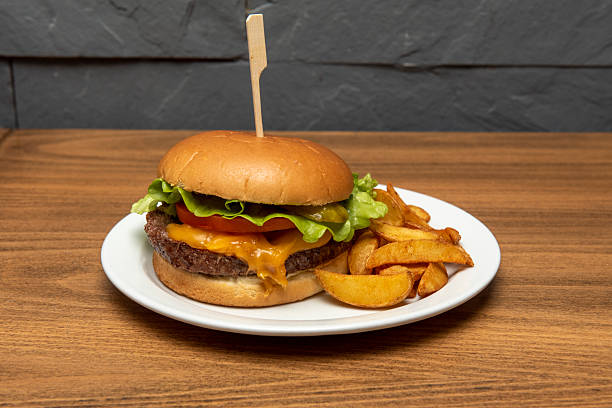 istock Classic beef burger with melted cheddar cheese, tomato, iceberg lettuce, pickled gherkins with wedge fries 2238822740