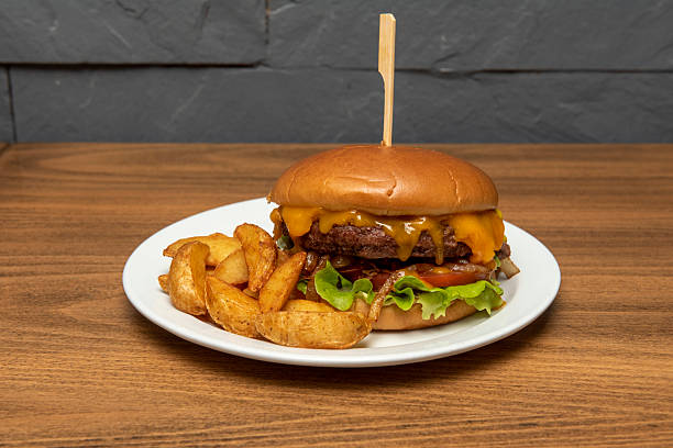 istock Charcoal-grilled beef burger with dripping melted cheddar cheese, caramelized onion, tomato and mustard with wedge fries 2238822959