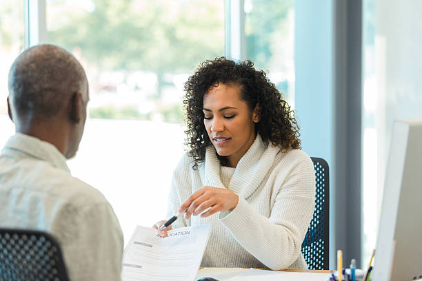 istock Woman guides man through application process with pen and paperwork in bright office. 2238826365