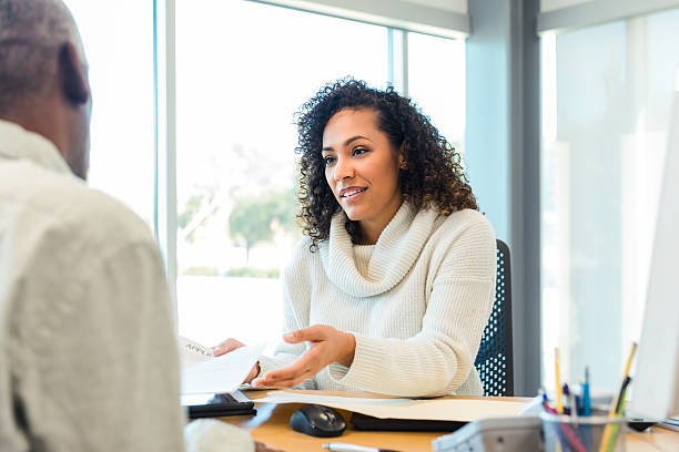 istock Mid-adult woman engaged in conversation while discussing documents with an unrecognized person indoors. 2238826380