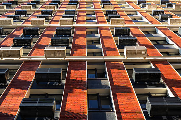 The image shows a close-up of a modern red brick building facade with visible air conditioning units in daylight.