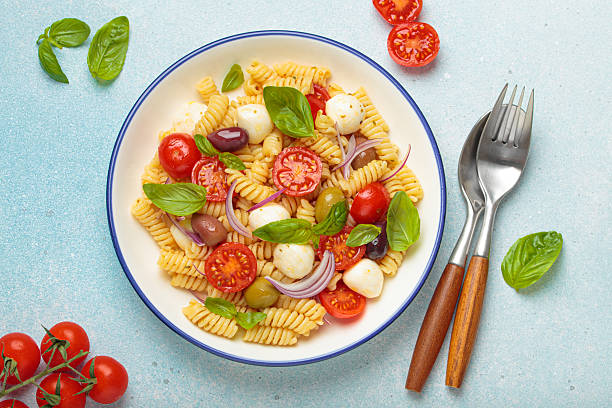 Italian pasta salad with fusilli, cherry tomatoes, mozzarella, olives, basil on blue background top view, Italian cuisine