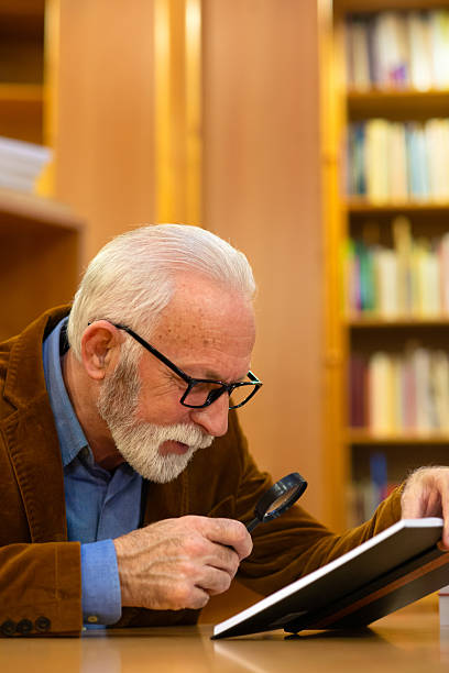 istock Senior man reading book in the library 2238874362