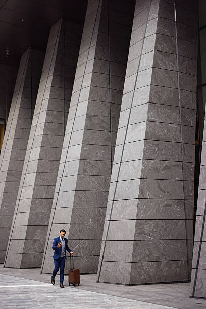 istock Businessman walking with suitcase and using smartphone near modern building 2238885971