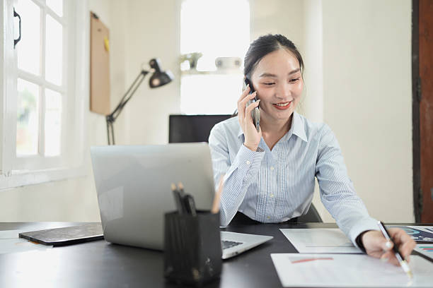 istock Asian businesswoman talking on cell phone while analyzing documents and working on laptop in office. 2238888612