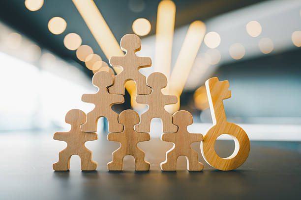 Wooden human figures forming a pyramid with a key symbol, representing teamwork, leadership, success, and human resources. Ideal for business concepts, strategy, or collaboration themes.