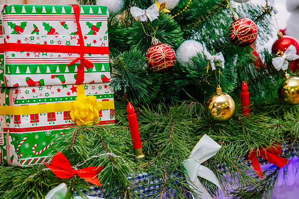 Festive Christmas scene with wrapped presents, colorful ribbons, baubles, and evergreen branches, creating a joyful holiday atmosphere under the tree.