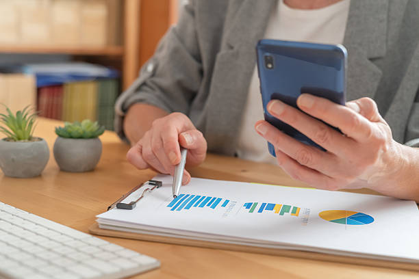 istock Business professional pointing with a pen at charts and graphs while holding a smartphone, analyzing financial reports, market trends, revenue growth and investment data on desk 2238892079