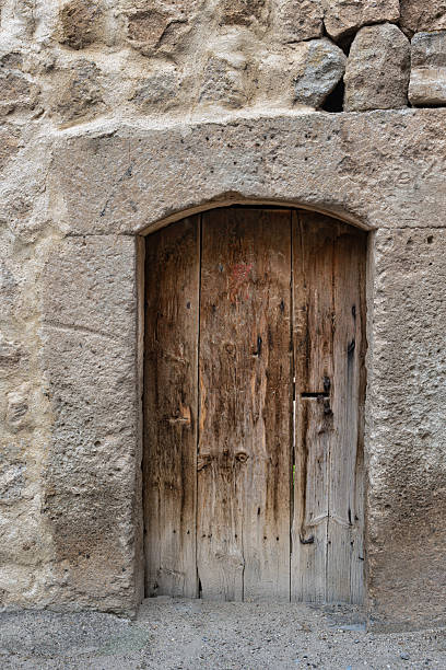 istock Weathered Wooden Door with Arched Stone Frame in an Ancient Stone Wall 2238896411
