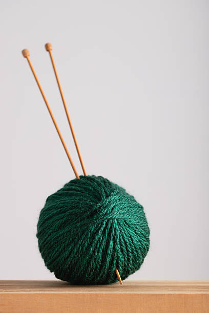 A knitting project featuring sparkling green yarn, surrounded by colorful yarns and knitting needles, set against a clean white background, showcasing creativity and craftwork