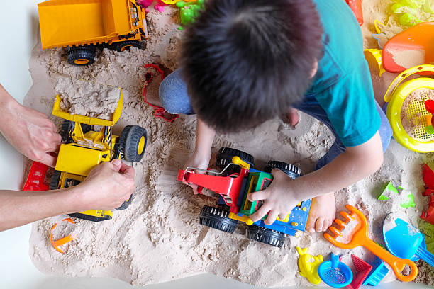 Top view child playing with toy construction trucks in sand, Montessori activity for kids, concept of creativity, sensory play, learning development, imagination, fun childhood, motor skills practice
