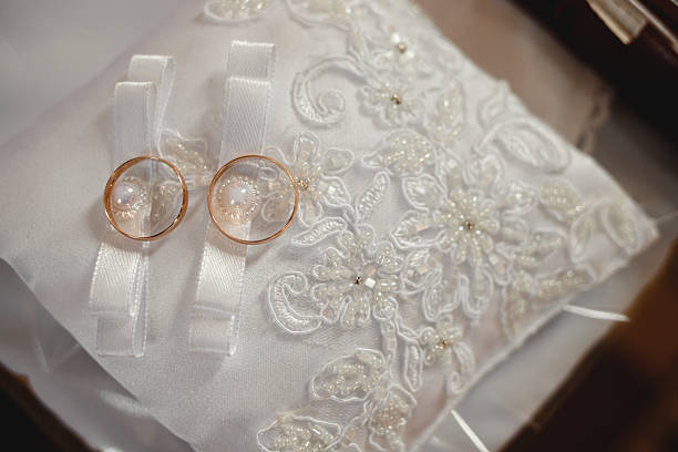 Close up detail of two shiny gold wedding bands resting on the beautiful lace and beaded embroidery of a ring cushion.
