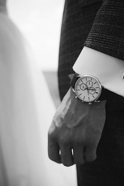 A sharp monochromatic close-up highlighting a gentleman's dress watch against a crisp white shirt and dark suit jacket.