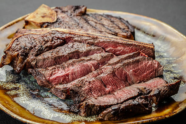 Close up of juicy grilled beef steak T-bone sliced medium rare and served on a ceramic plate. Perfect gourmet meat dish for steakhouse, barbecue, restaurant menu, or culinary advertising