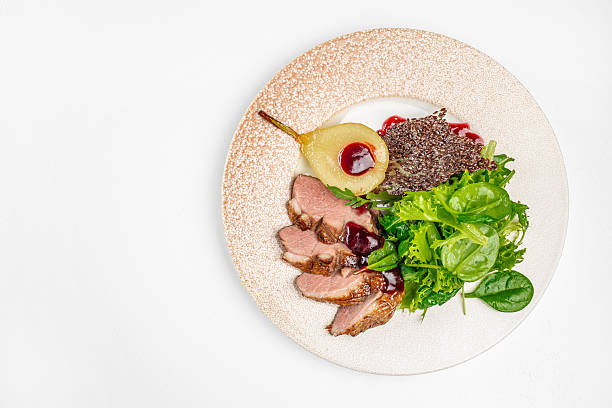Elegant gourmet dish of roasted duck breast served with caramelized pear, fresh green salad mix, berry sauce and crispy garnish. festive menus, or gourmet food concepts