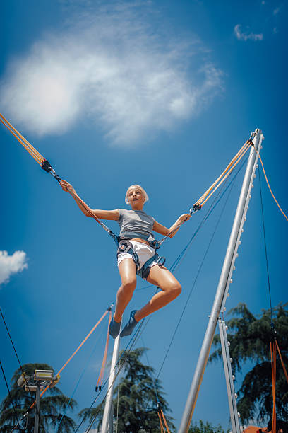 Girl having fun jumping high on bungee trampoline with safety equipment, enjoying summer activity under a beautiful blue sky
