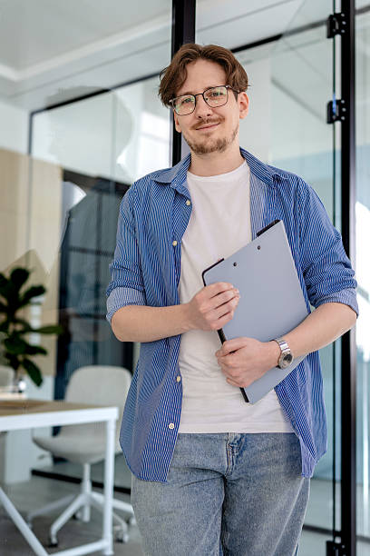 istock Young businessman smiling in modern office while holding clipboard and working on freelance projects 2238914675