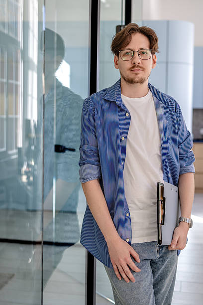 istock Young businessman stands confidently in modern office setting with documents 2238914738
