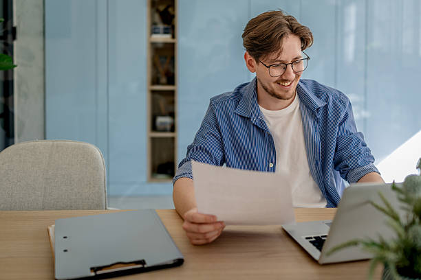 istock Young entrepreneur working with confidence at modern office desk, smiling while reviewing documents on laptop 2238914855