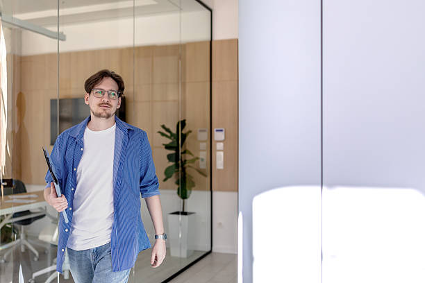 istock Young man confidently walks through modern office space carrying a clipboard while engaging in business activities 2238914933