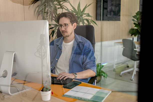 istock Young man engaged in freelance work at a modern office space with plants and technology 2238915375
