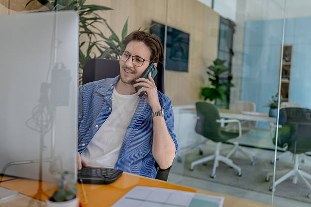 istock Young man happily working at his desk in a modern office while talking on the phone and engaging with technology 2238918520