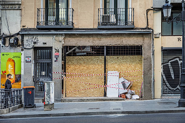 Madrid, Spain, Europe, September 10, 2025: A closed retail storefront in central Madrid, Spain, is boarded up with plywood and marked by red-and-white caution tape, indicating ongoing renovation or construction. The facade includes a large opening filled with debris and building materials, while adjacent businesses remain shuttered..