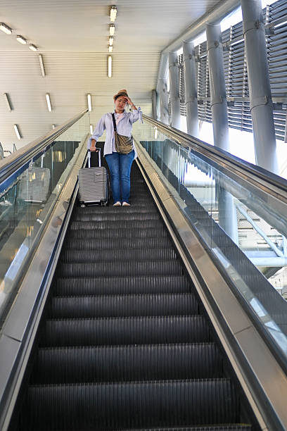 A weary woman on the escalator touches her forehead, struggling with fatigue and headache before boarding.