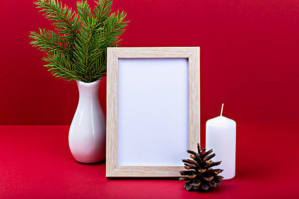 istock Decorative arrangement with empty frame, candle, pine cone and evergreen plant on red background 2238923577
