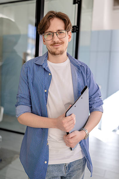 istock Young white man smiling while working in a modern office environment with a file folder in hand 2238926212
