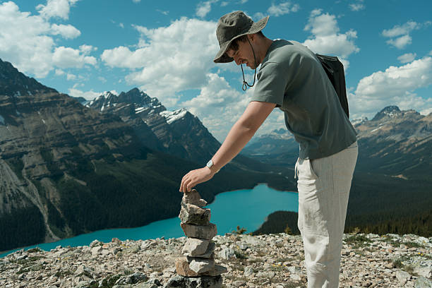 Hiker stacking stones at scenic mountain overlook with turquoise lake.