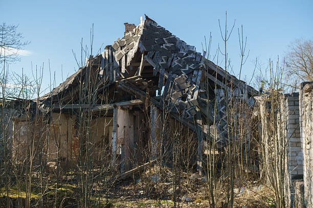 Ruins of a large, abandoned brick mansion with a turret and columned facade, set against a clear blue sky. A scene of historical decay and forgotten grandeur