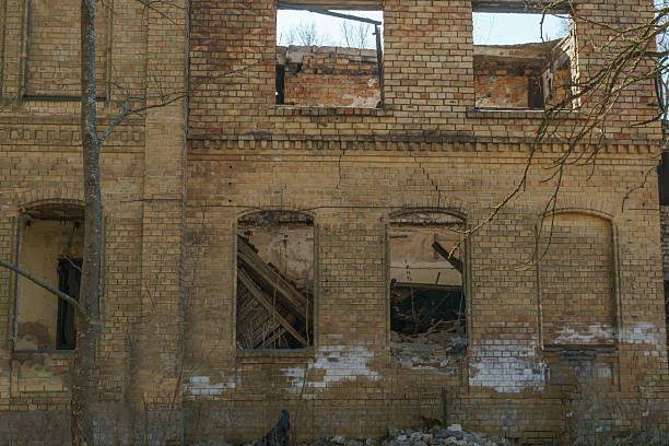 Ruins of a large, abandoned brick mansion with a turret and columned facade, set against a clear blue sky. A scene of historical decay and forgotten grandeur