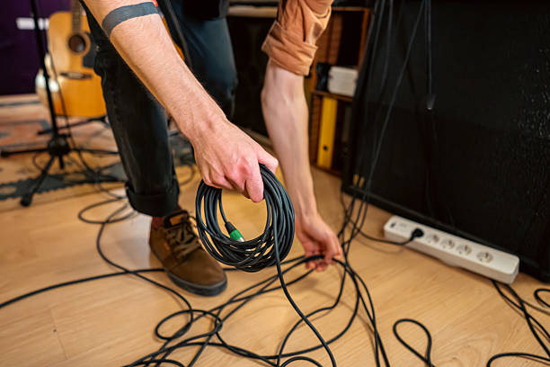 A close-up view of the stage floor. Several thick black and colored instrument cables are tangled together, overlapping in random loops across the worn stage surface. There are no visible instruments or musicians yet—only the chaotic, raw setup that forms the foundation of live music. This image captures the behind-the-scenes energy, where every cable carries the potential of rhythm, melody, and noise.