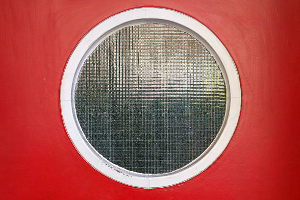 istock Round textured glass window in white frame on red painted door, close-up view 2238938298