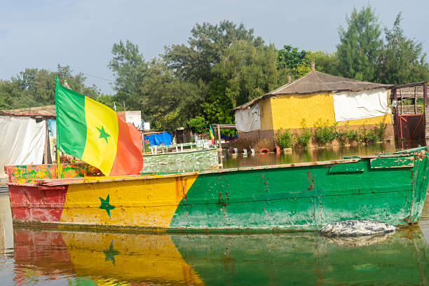 A vibrant boat adorned with the Senegalese flag gently floats on the water, creating a picturesque scene in a quaint village, reflecting the local culture and heritage.